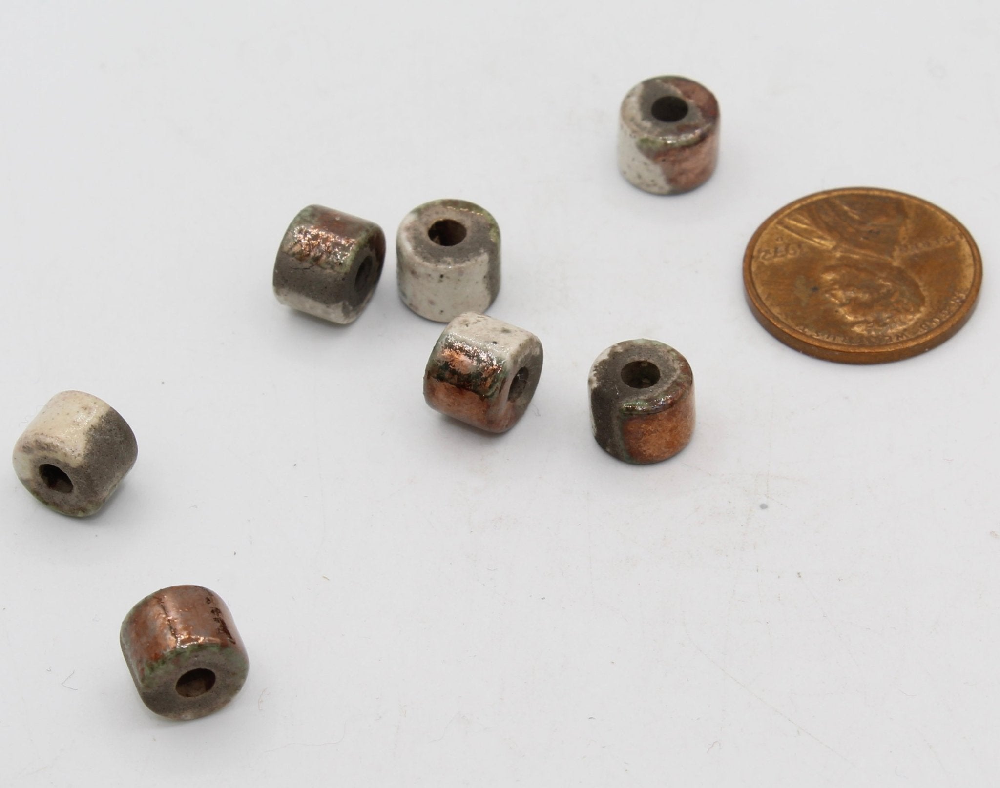 Small metal beads on a white background with a penny for scale